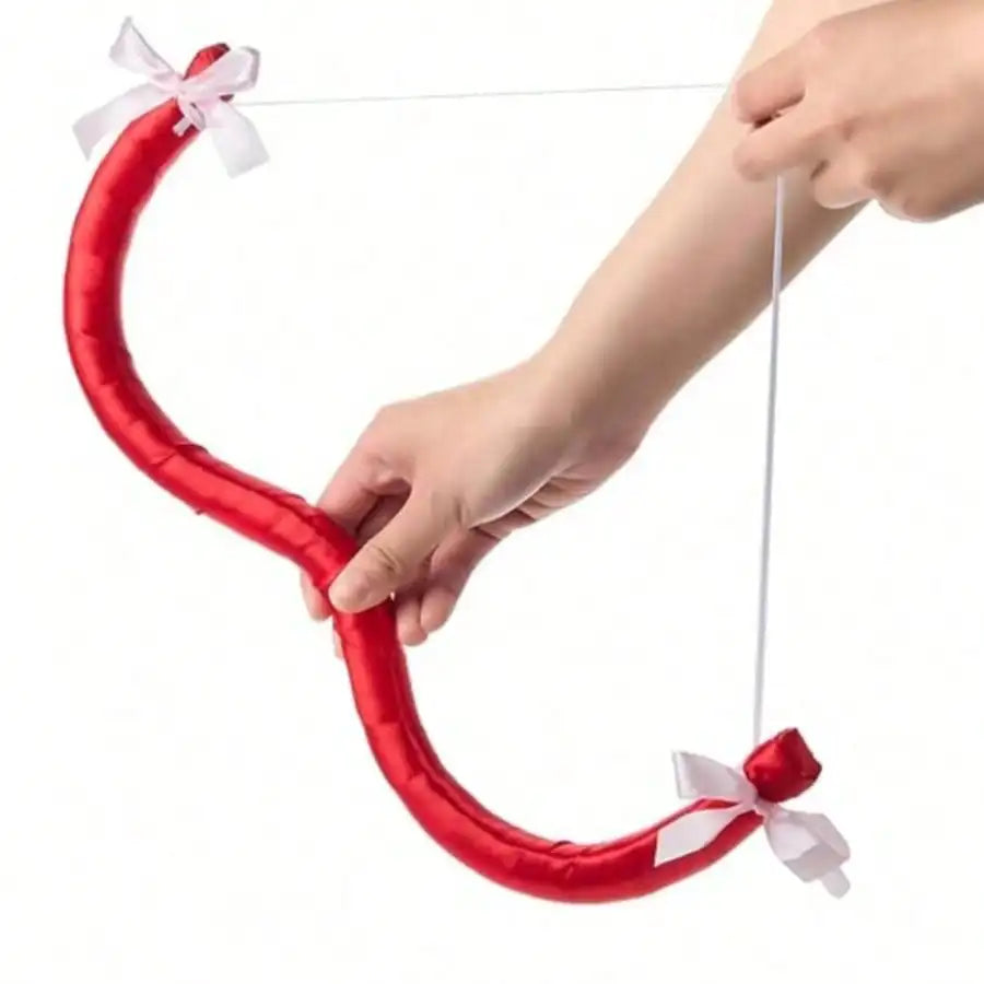 A hand is holding a red, curved bow and arrow prop with a white ribbon for costumes and parties.