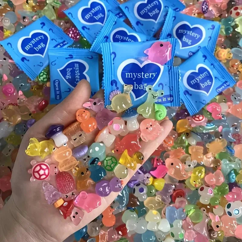 A hand holds numerous glow in the dark resin decor pieces, including small animals and shapes, alongside packaged mystery bag