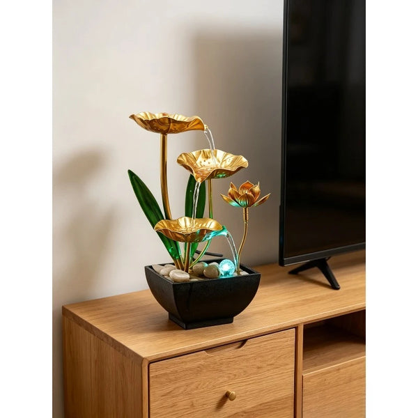 A golden lotus pond tabletop water fountain with green leaves and blue water sits on a wooden cabinet.