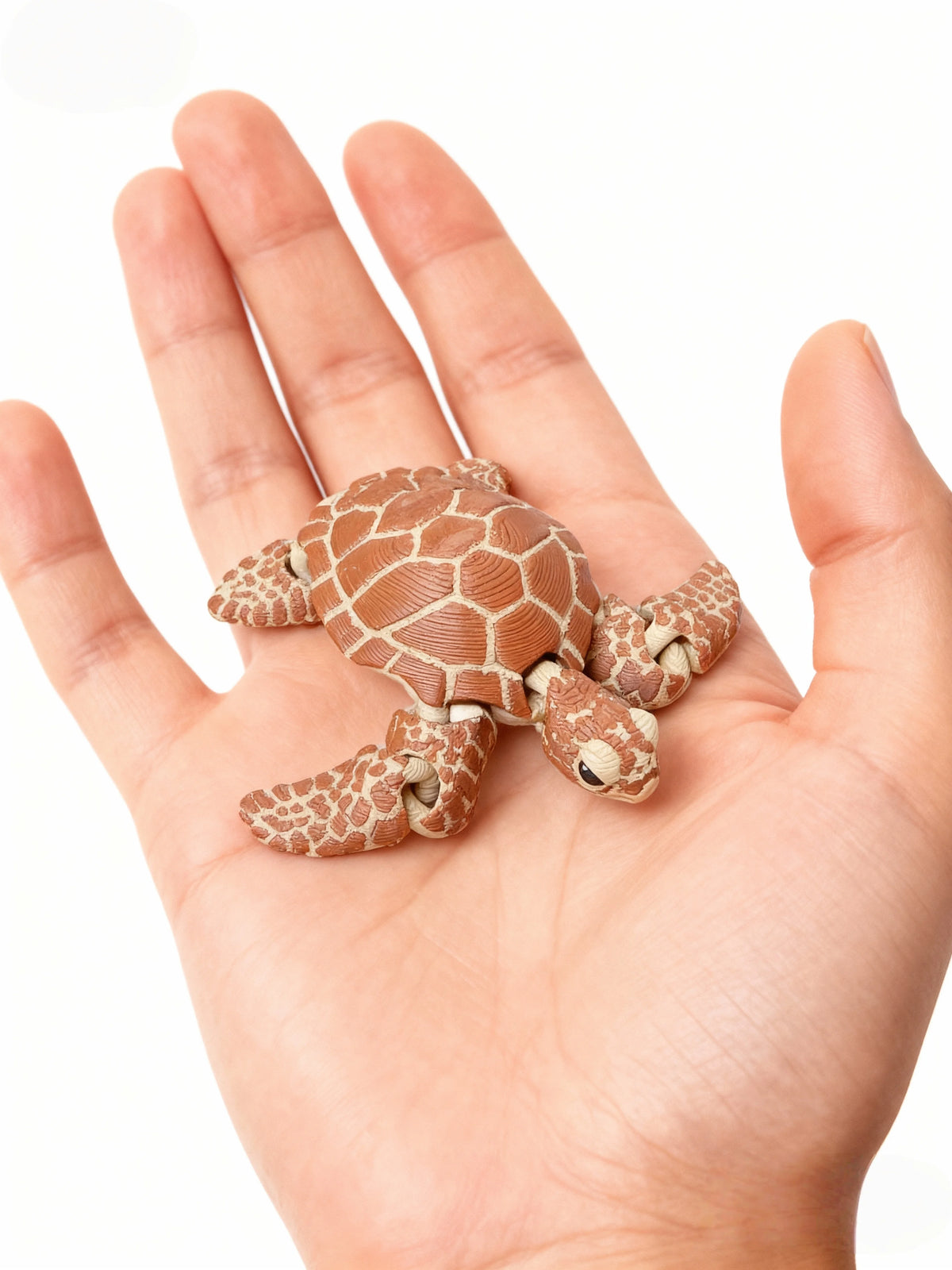A hand holds a small, brown, 3D printed articulated turtle figurine decoration.