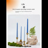 A set of gradient blue taper candles displayed on natural wood and moss in a minimalist setting.