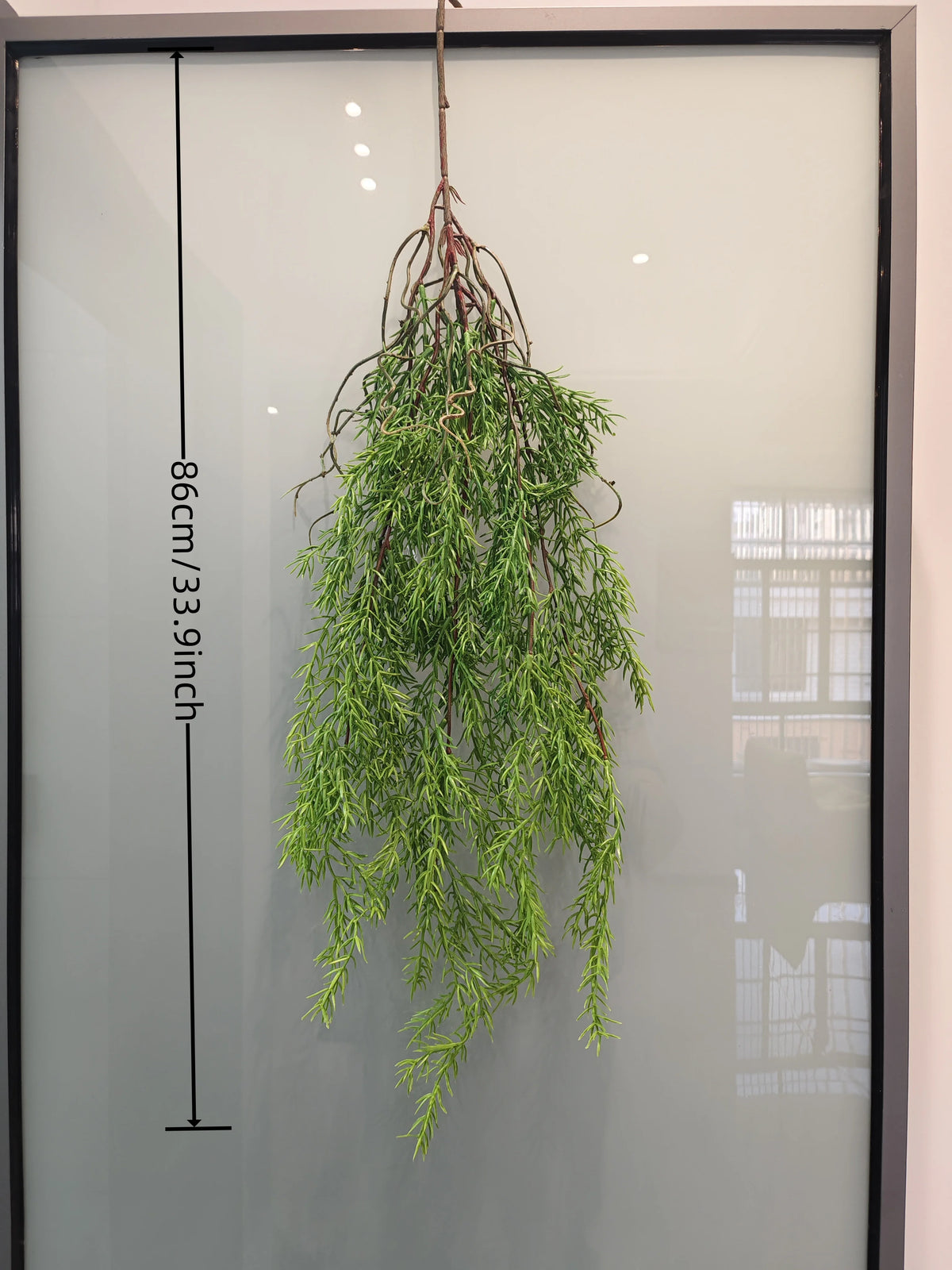 Artificial hanging ivy vine with reddish roots displayed against a glass background.