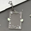 A clear acrylic photocard holder keychain with a star charm and decorative elements is displayed on a dark gray surface.