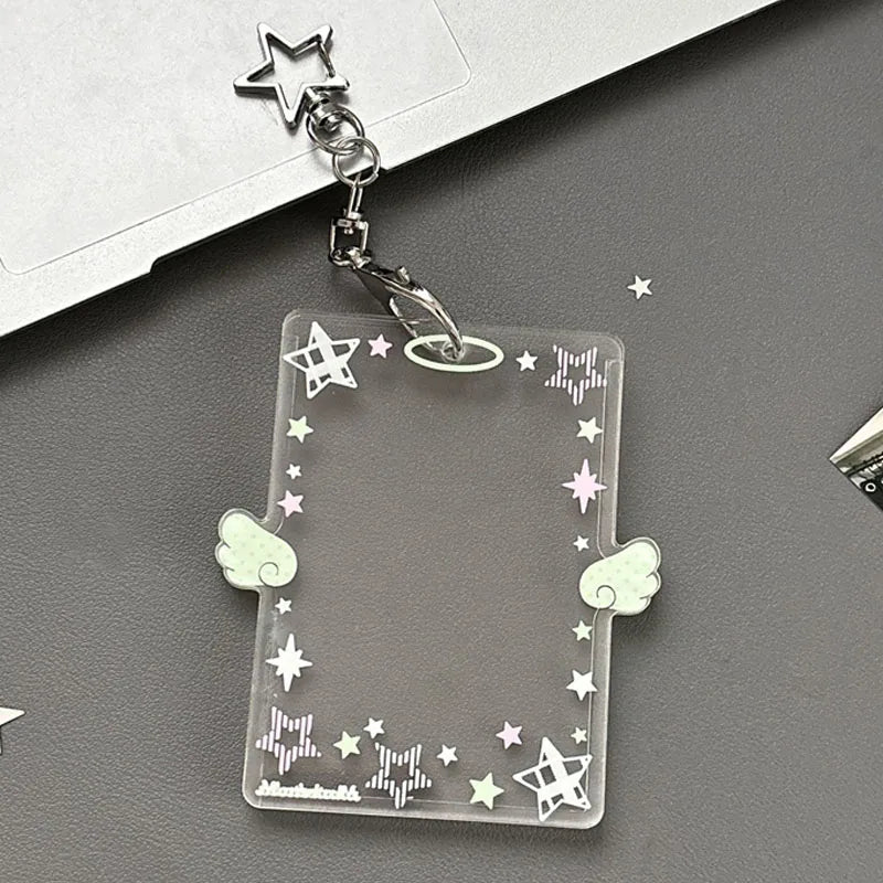 A clear acrylic photocard holder keychain with a star charm and decorative elements is displayed on a dark gray surface.