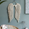 Handwoven angel wing macrame wall hanging in cream color displayed on a gray wall.