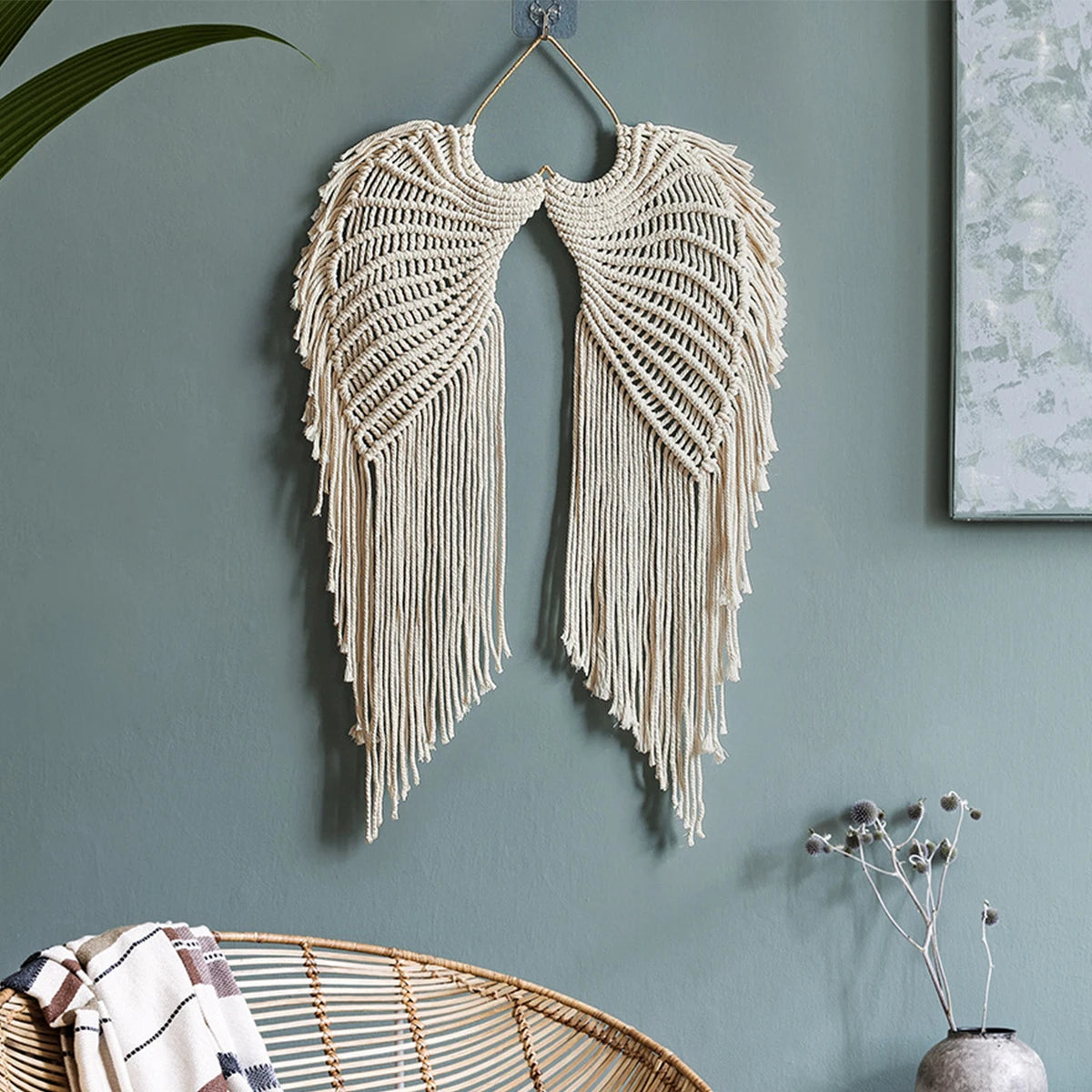 Handwoven angel wing macrame wall hanging in cream color displayed on a gray wall.