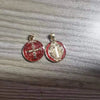 A pair of gold-toned religious pendants featuring a cross and a depiction of St. Benedict on red circular medallions.