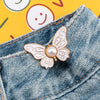A gold-toned butterfly clip is fastened onto the denim fabric of a pair of jeans.