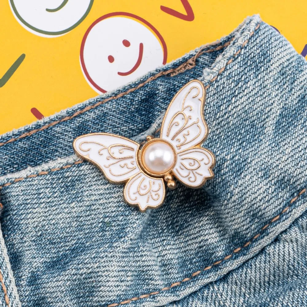 A gold-toned butterfly clip is fastened onto the denim fabric of a pair of jeans.