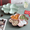 A heart-shaped four-compartment tray filled with various dried snacks like nuts and seeds on a gray surface.