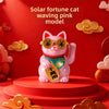 A pink cat ornament with gold accents and a green collar is displayed on a red circular base.