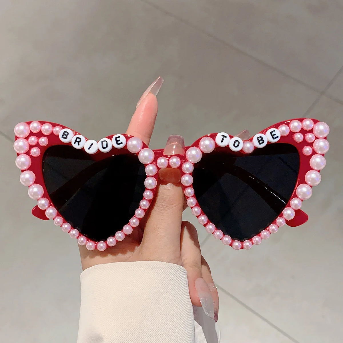 A pair of heart-shaped sunglasses decorated with pink pearls and the word bride to be