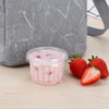 A clear disposable dessert cup filled with pink strawberry smoothie sits on a wooden surface next to fresh strawberries.