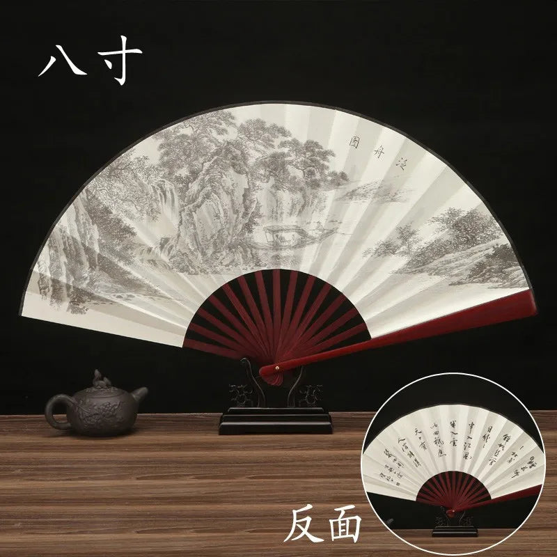 A black and white decorative folding fan with a landscape design is shown, along with a small bronze teapot.