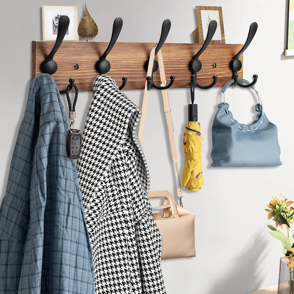 A wooden wall-mounted coat rack with five black hooks displaying various coats and bags.