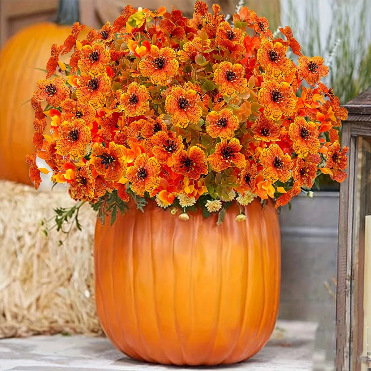An orange pumpkin vase filled with bright orange and yellow artificial autumn flowers.