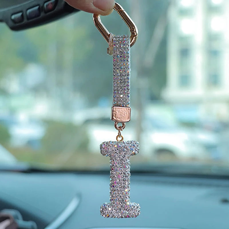 A close-up of a crystal letter keychain charm hanging from a gold-colored ring.