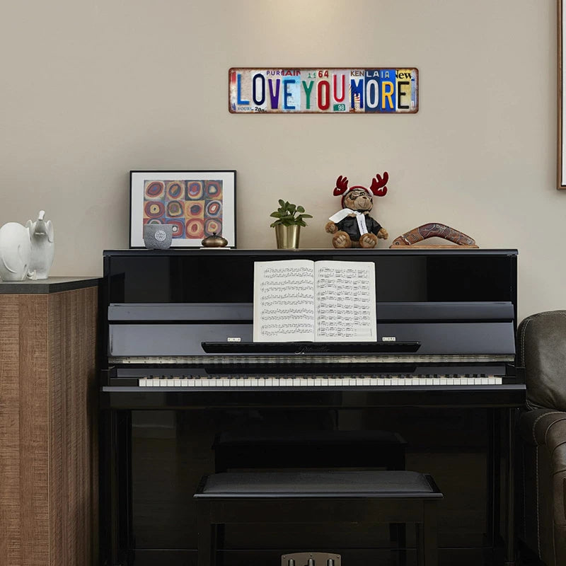 A vintage metal street sign decor featuring the text LOVE YOU MORE mounted on a light wall above a black piano.