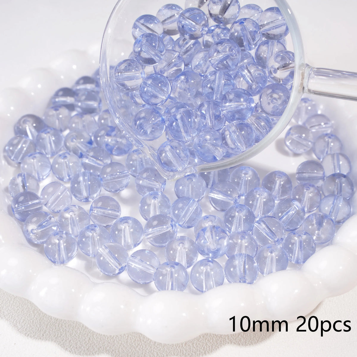 A clear glass magnifying glass shows small round blue spacer beads scattered on a white dish.