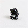 A small black and white resin keychain shaped like a cat with pink accents.