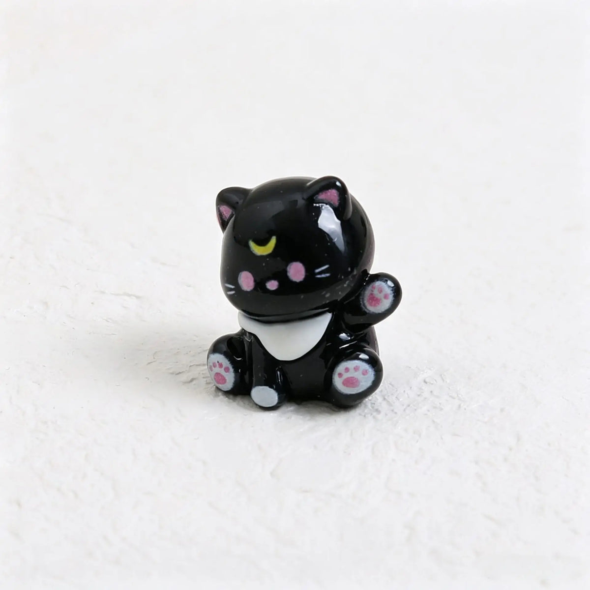 A small black and white resin keychain shaped like a cat with pink accents.