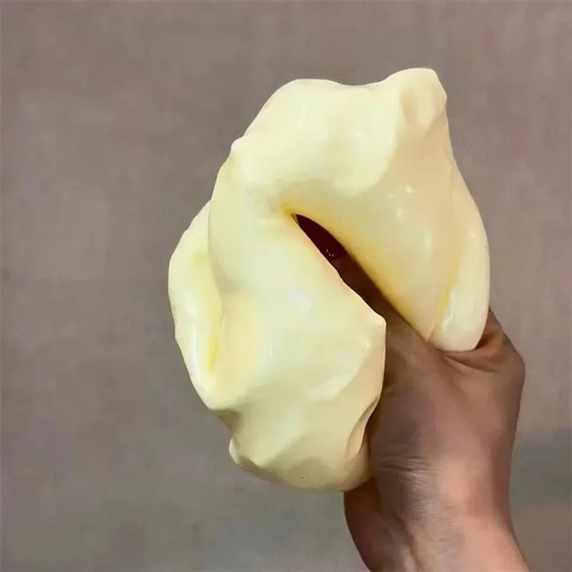 A hand is holding a pale yellow, squishy stress relief toy shaped like cheese.
