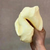 A hand is holding a pale yellow, squishy stress relief toy shaped like cheese.