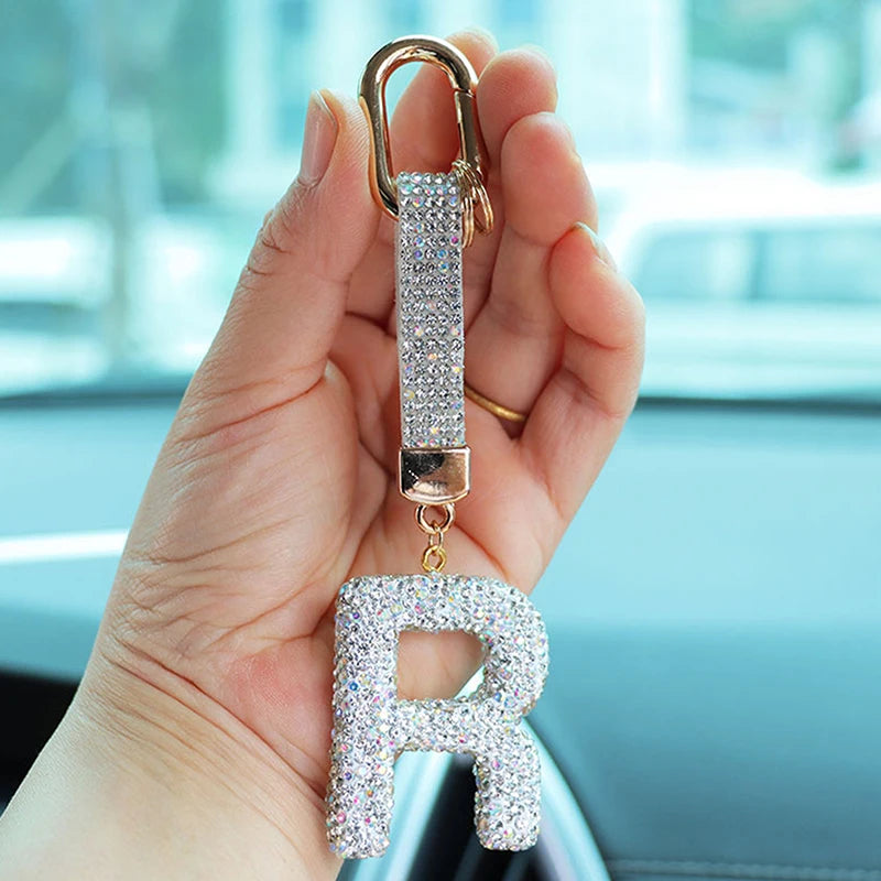 A hand holds a crystal letter keychain charm shaped like the letter R with a gold clasp.