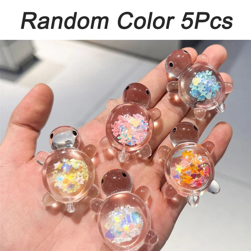 A hand holds five glow-in-the-dark mini sea turtle figurines with colorful glitter inside for DIY crafts