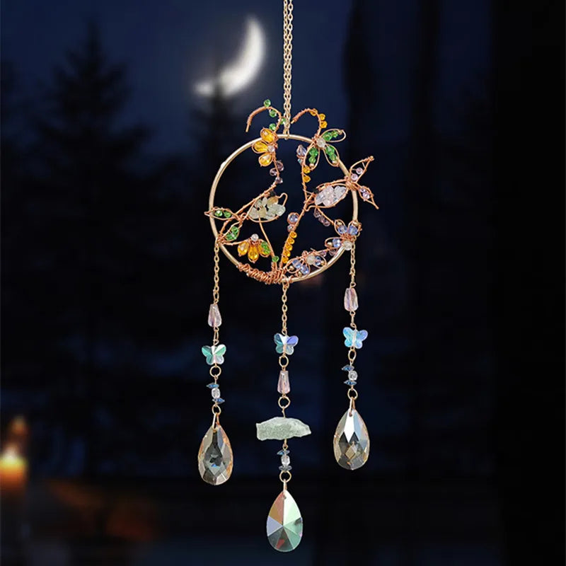 A hanging crystal tree of life sun catcher featuring gold wire and various colored crystals and leaves against a dark backgro