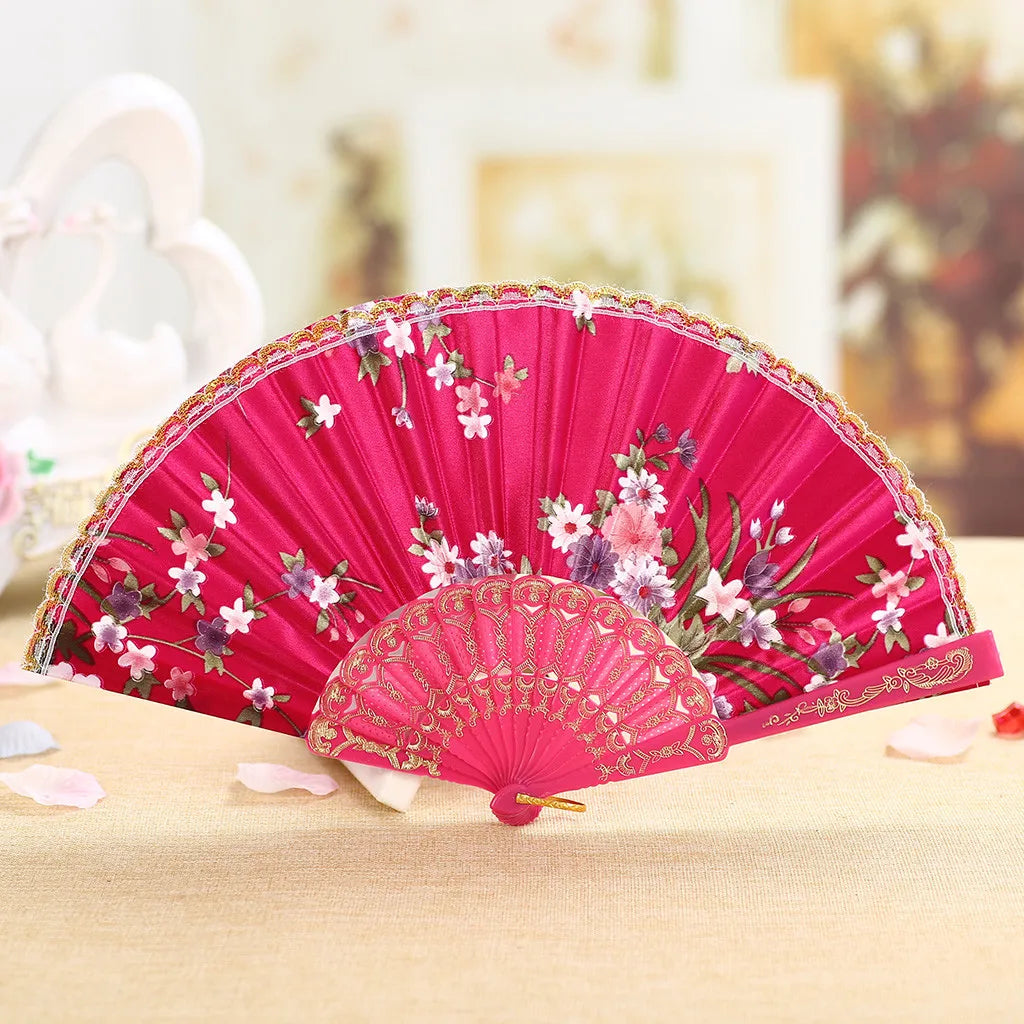 A vibrant pink vintage lace hand fan with floral embroidery is displayed on a light wooden surface.