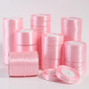 Pink silk satin ribbons stacked in rolls and a loose coil for crafting