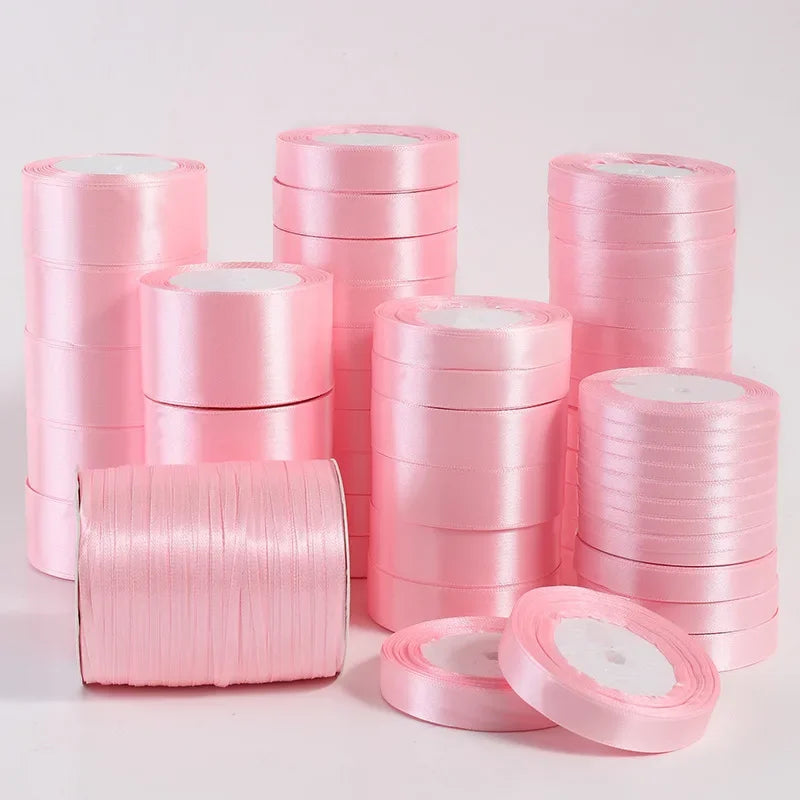 Pink silk satin ribbons stacked in rolls and a loose coil for crafting