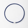 A dark blue handmade string bracelet with a gold plated clasp laid flat on a white background.