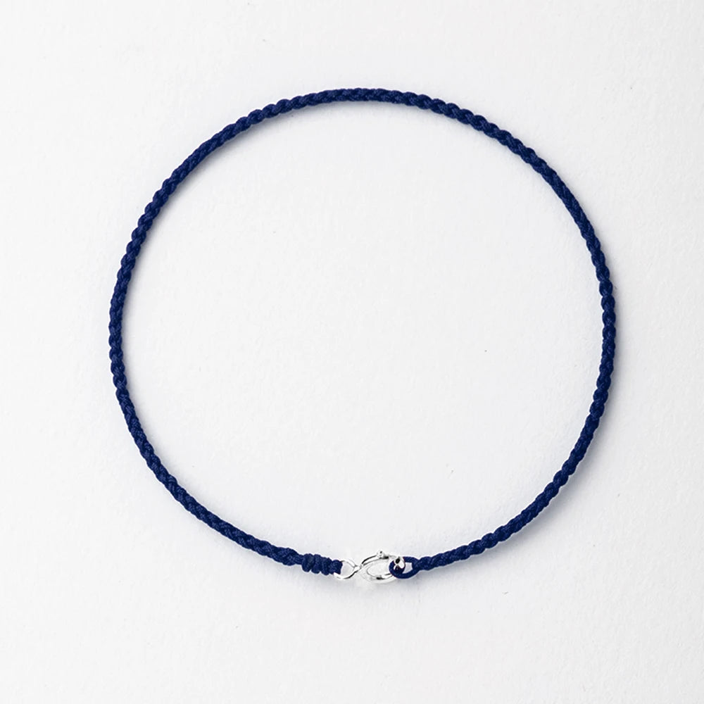 A dark blue handmade string bracelet with a gold plated clasp laid flat on a white background.