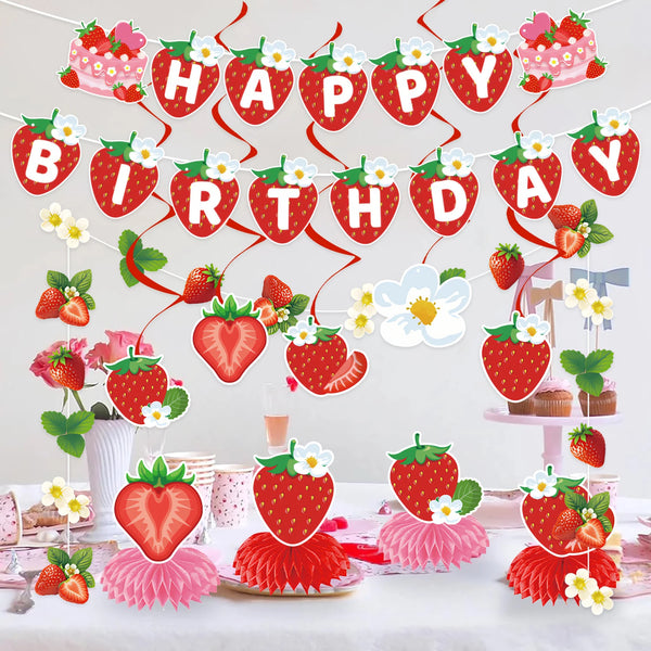 A strawberry theme birthday party decoration set featuring a banner and honeycomb ornaments on a white table.