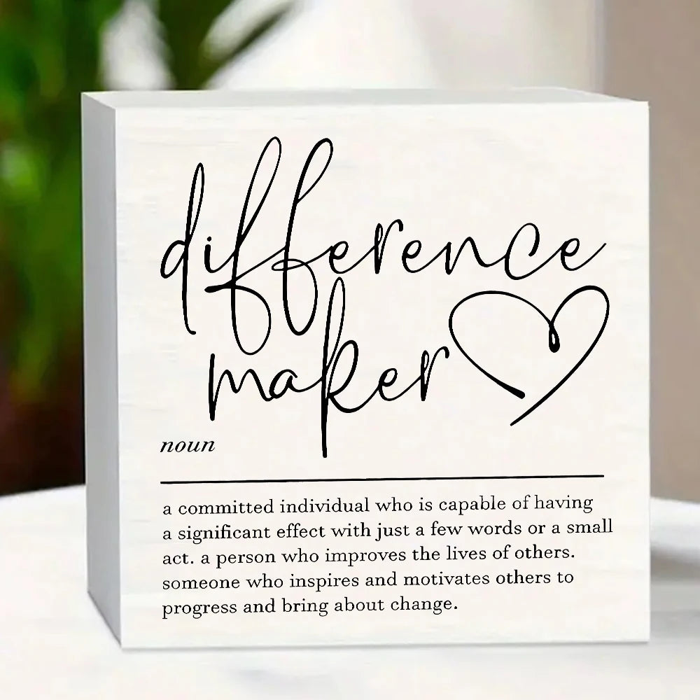 A white wooden sign with black script that reads difference maker and a definition below.