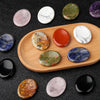 A collection of oval natural stone beads in various colors including pink, white, green, orange, and blue arranged on a woode