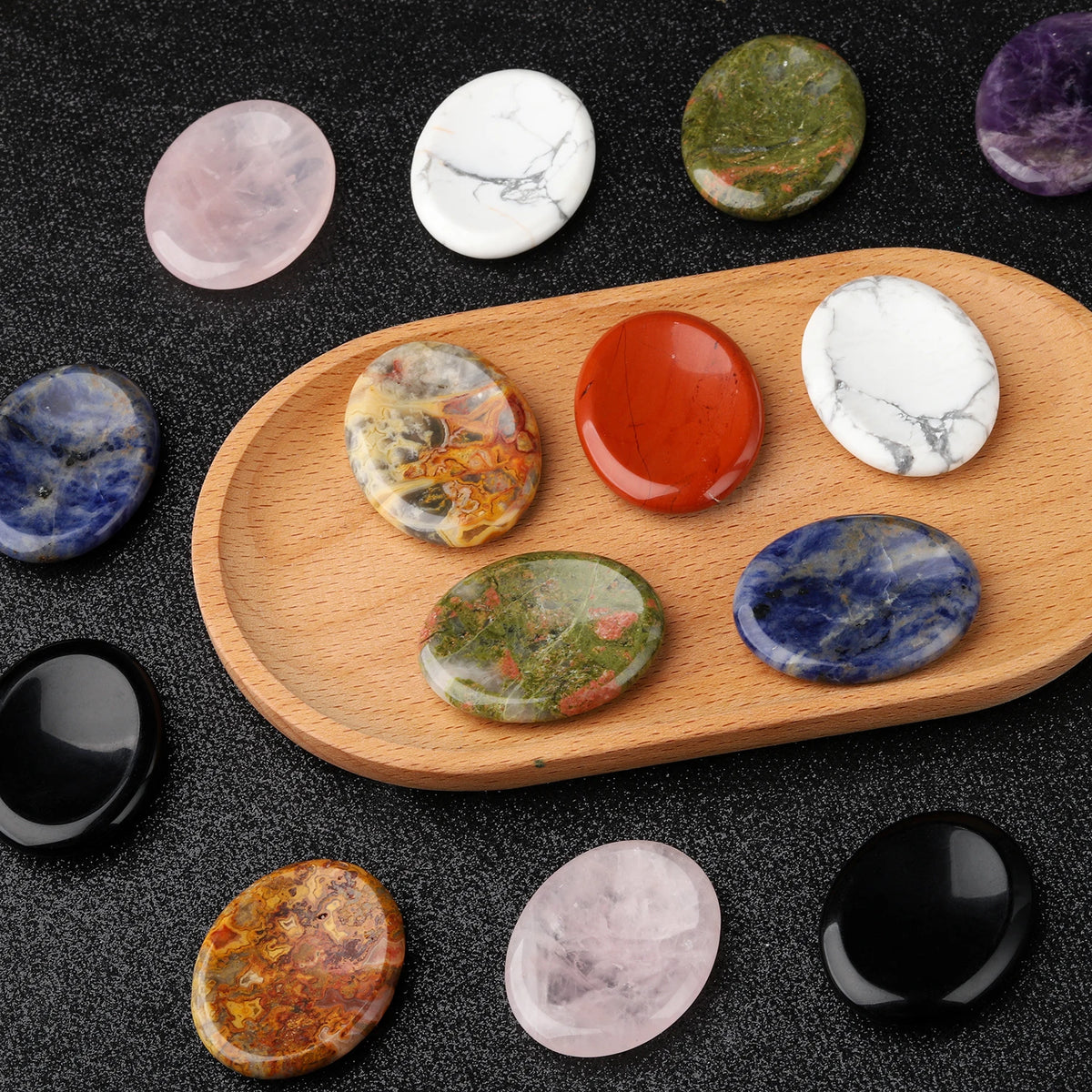 A collection of oval natural stone beads in various colors including pink, white, green, orange, and blue arranged on a woode