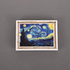 A framed painting featuring a night sky with bright yellow stars and a dark landscape, used as a fridge magnet.