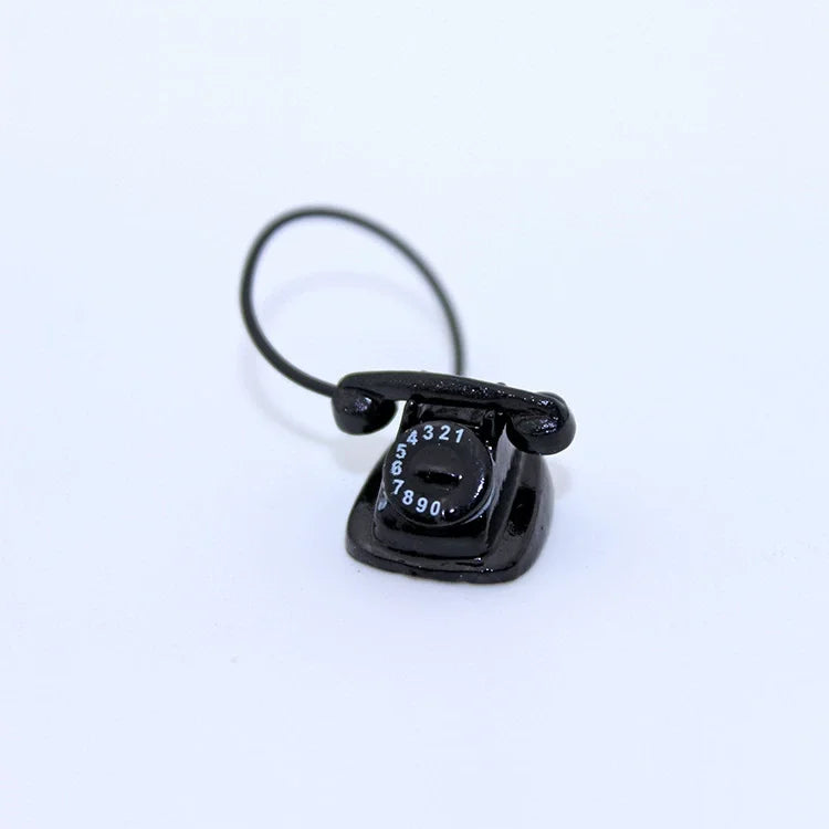 A black vintage rotary desk phone miniature decor with a coiled cord.