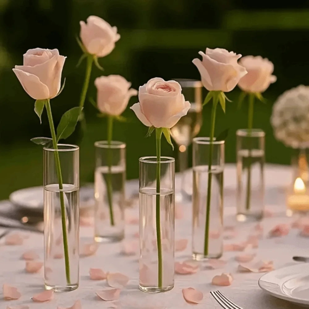 Several crystal clear cylinder vases holding pink roses on a white table.
