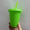 A hand holds a bright lime green plastic cold cup with a matching straw against a white background.
