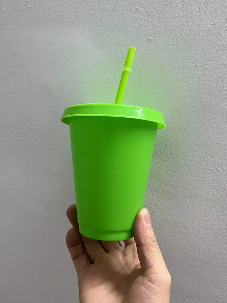 A hand holds a bright lime green plastic cold cup with a matching straw against a white background.