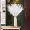 A vase holds a bouquet of white pampas grass stems displayed on a green cabinet door.