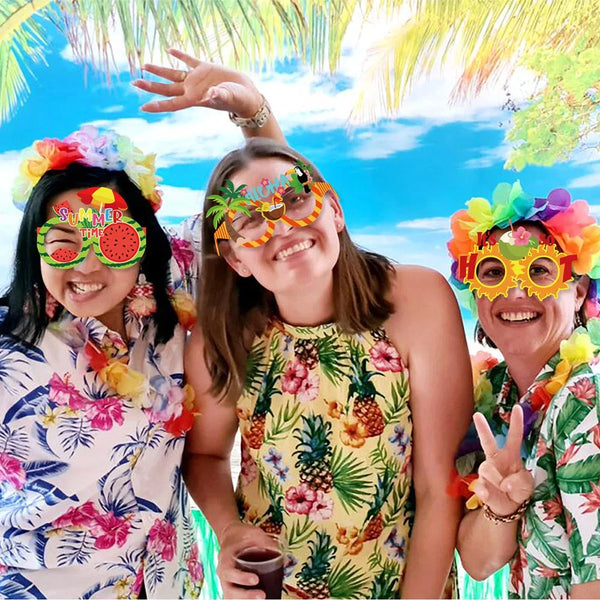 Three women smiling outdoors wearing colorful Hawaiian themed sunglasses and tropical floral shirts