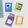 A collection of four magnetic photo frames in blue, green, purple, and yellow, displaying small photographs.