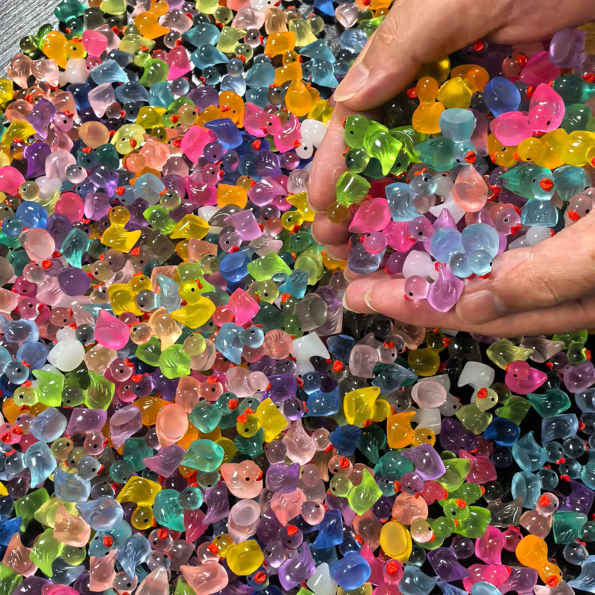 A hand is holding a pile of colorful luminous mini duck figurines for fairy gardens.