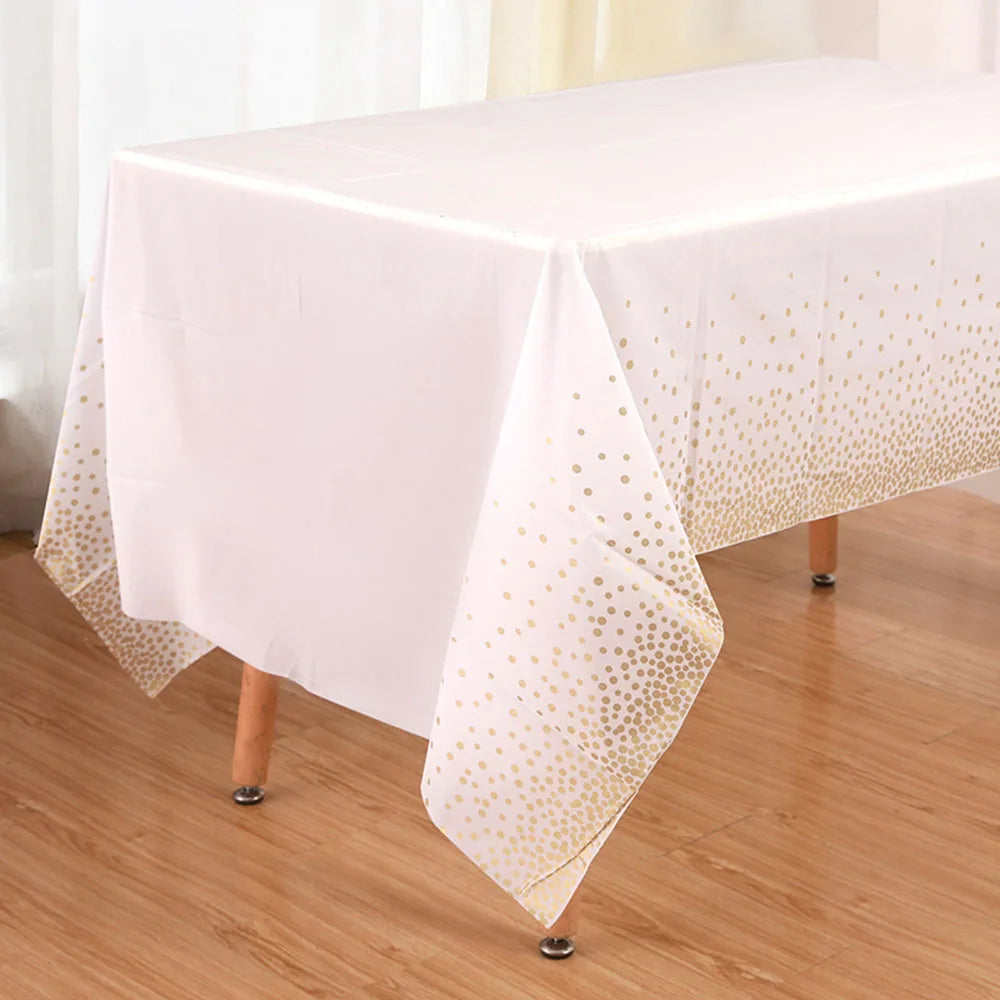 Una mesa de madera con mantel blanco de lunares dorados, preparada para una fiesta.