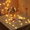 A close-up of battery-powered globe string lights illuminating a table with flowers and a decorative giraffe figurine.